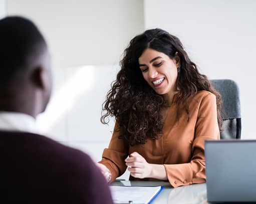 Smiling loan officer with curly hair discussing with client at desk with laptop.