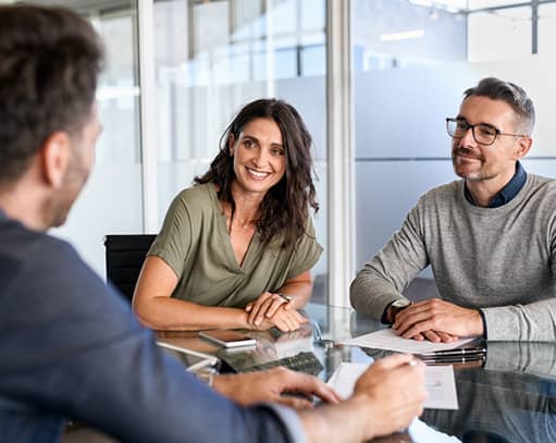 Three people in business meeting discussing documents at glass table in office.