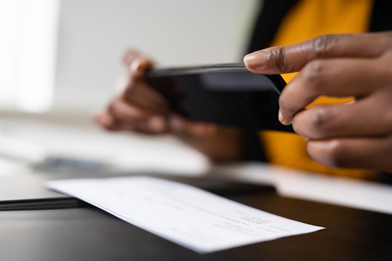 Woman using smartphone to photograph check for mobile deposit at desk.